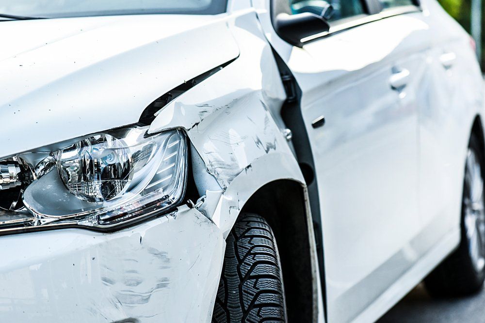 A White Car with A Damaged Front Bumper Is Parked on The Side of The Road — East Maitland Body Repairs in East Maitland, NSW