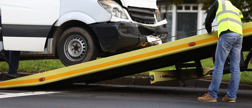A Tow Truck Is Towing a White Van with A Damaged Front End — East Maitland Body Repairs in East Maitland, NSW