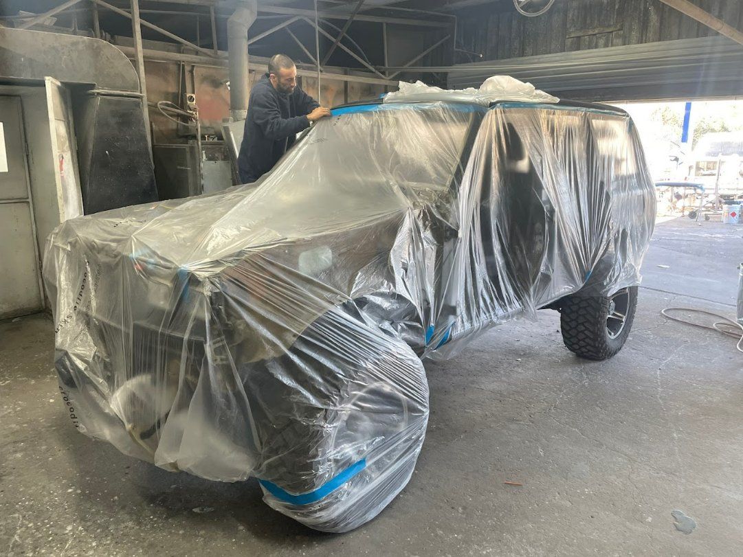 A Man Is Covering a Car with Plastic Wrap in A Garage — East Maitland Body Repairs in Raymond Terrace, NSW