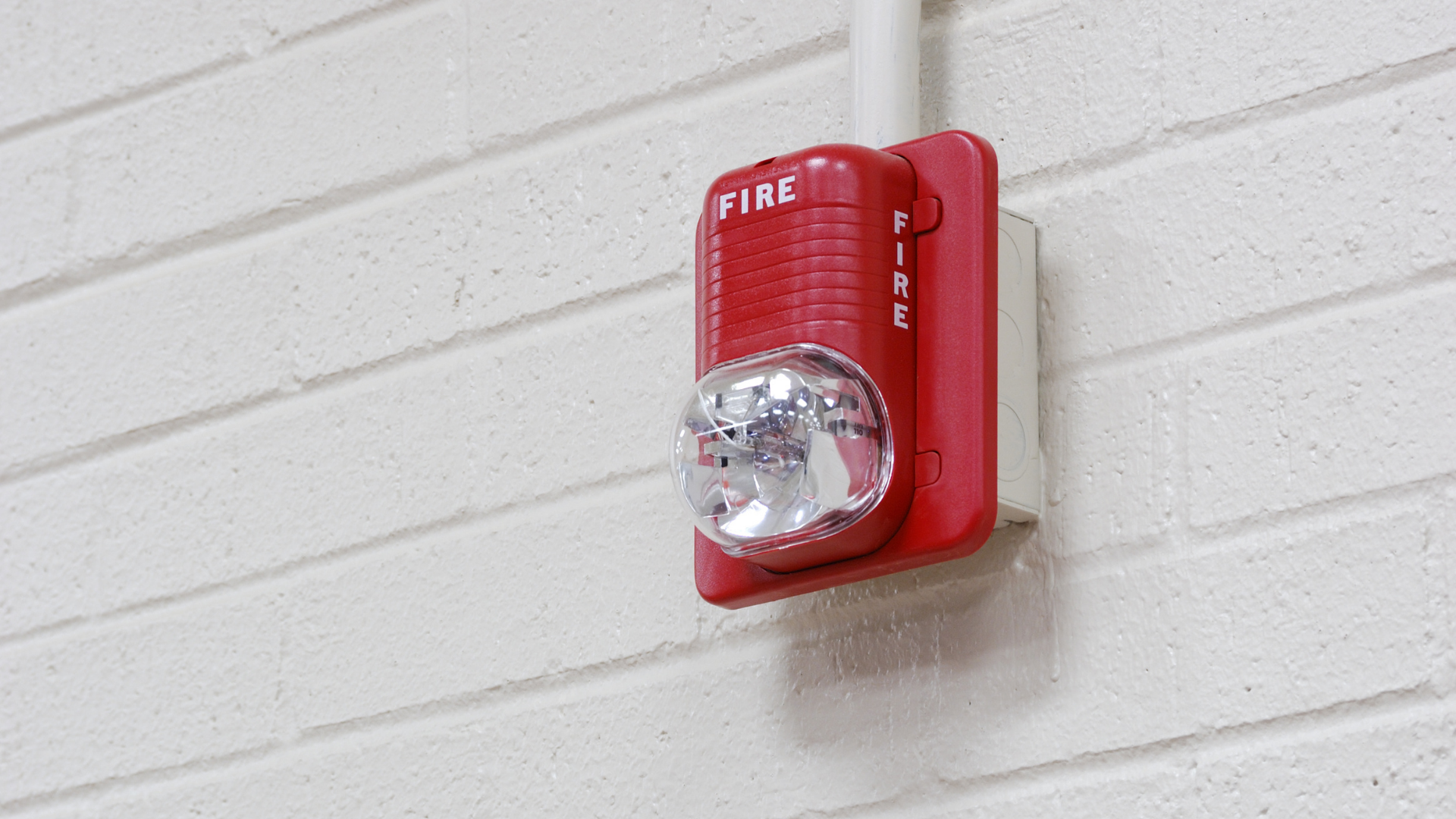 Red fire alarm mounted on a white brick wall.