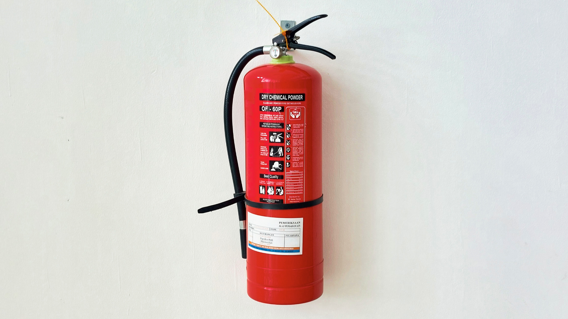 Red fire extinguisher mounted on a white wall with a black hose and label.