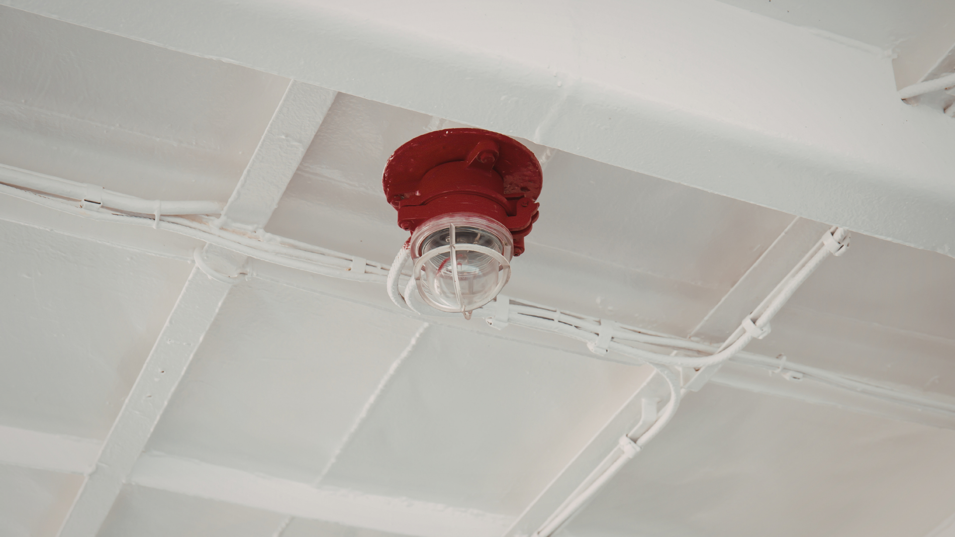 Red ceiling-mounted light fixture on a white ceiling with exposed beams.