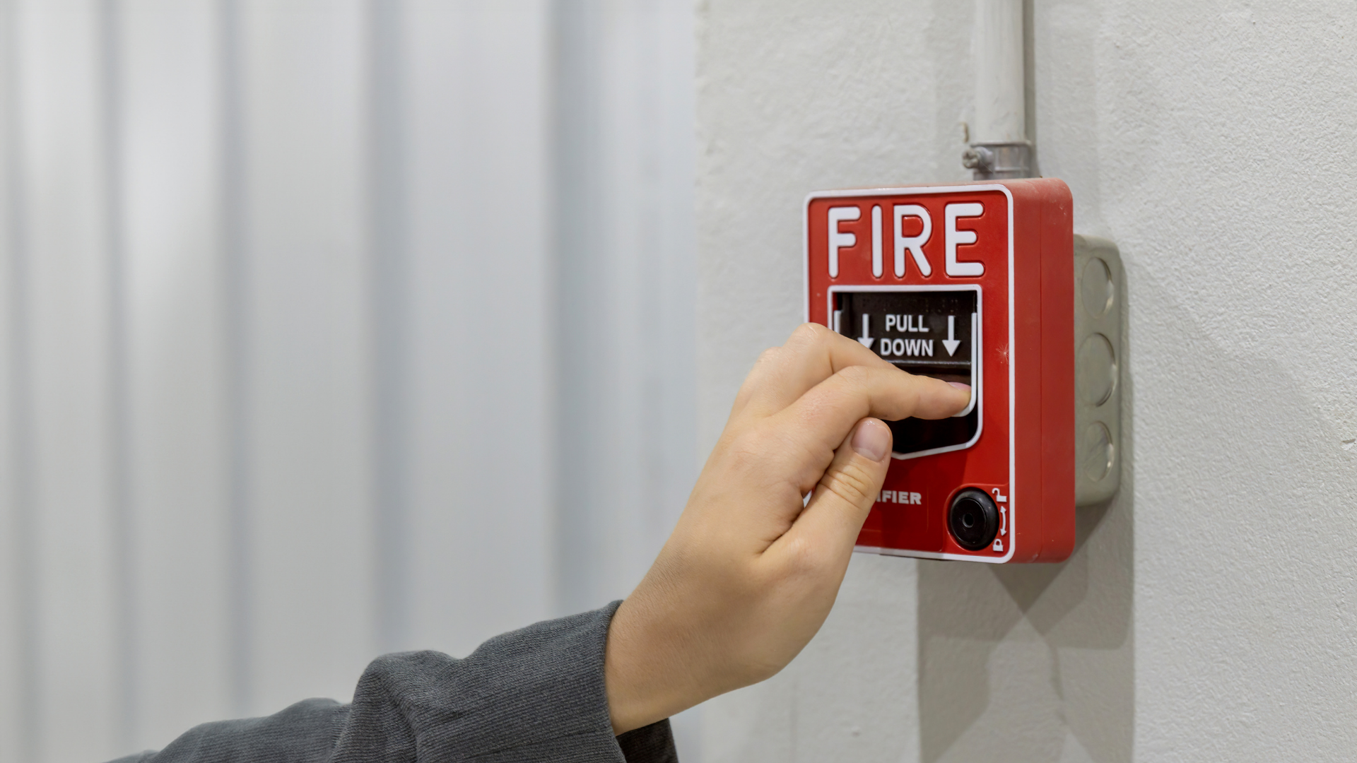Hand pressing a red fire alarm pull station on a wall