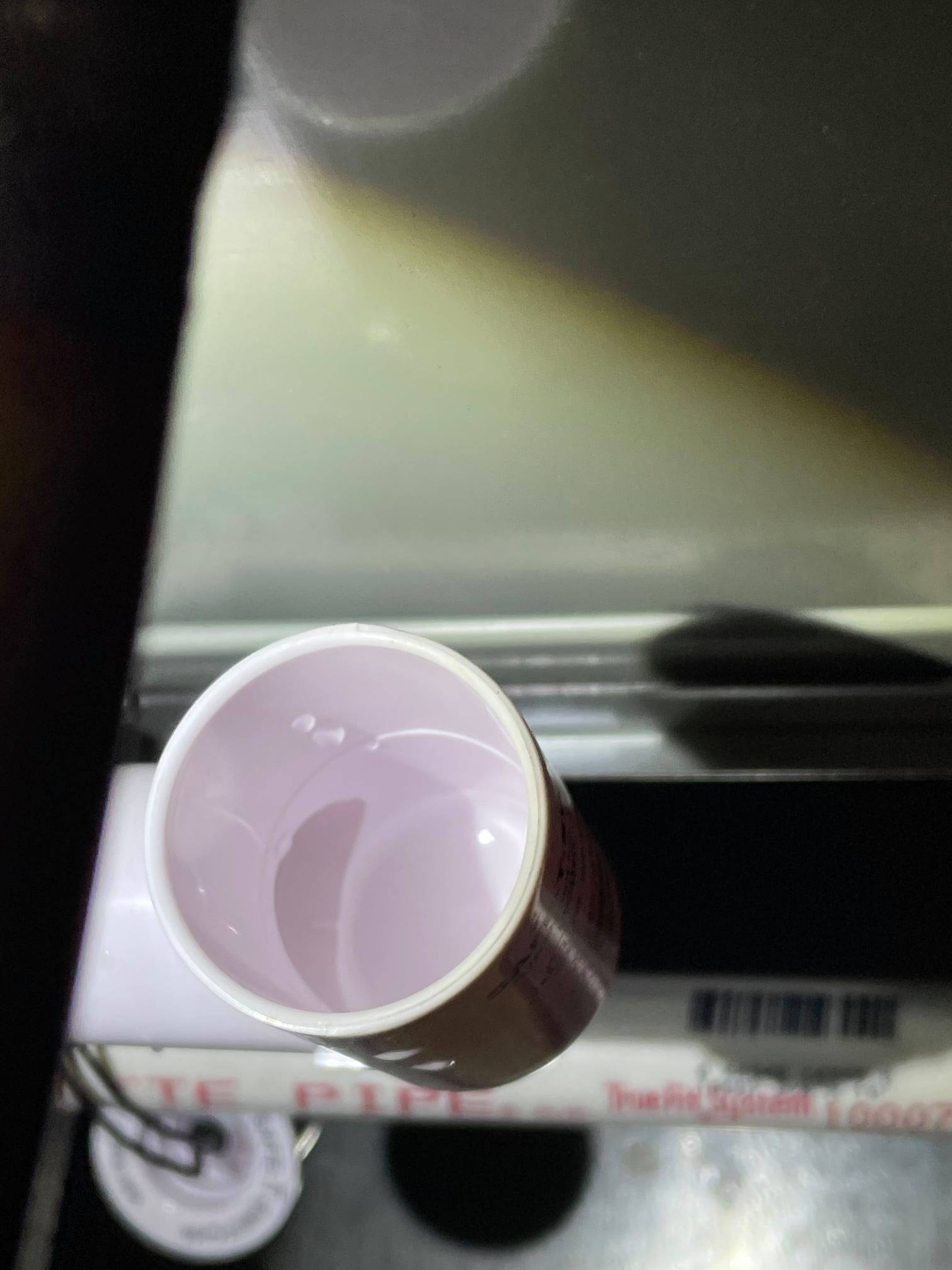 A top-down view of an open white PVC pipe fitting containing a small amount of liquid, with a larger pipe visible below.