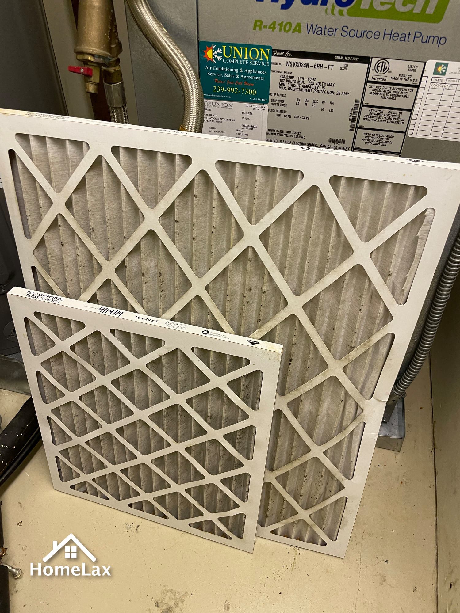 Two dirty pleated air filters of different sizes leaning against a Hydrotech HVAC unit.
