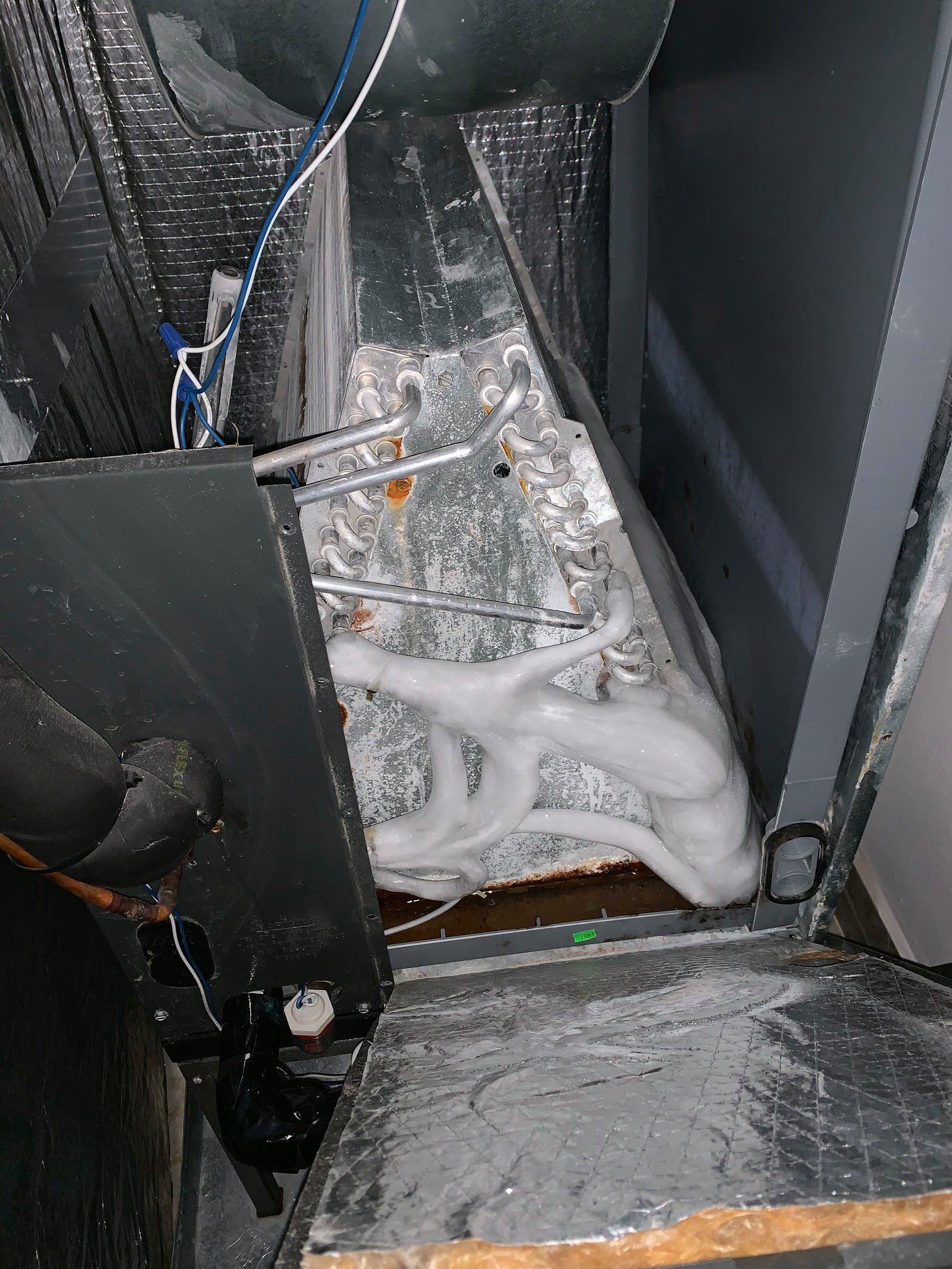An HVAC evaporator coil covered in thick, white ice, located inside an open metal unit.