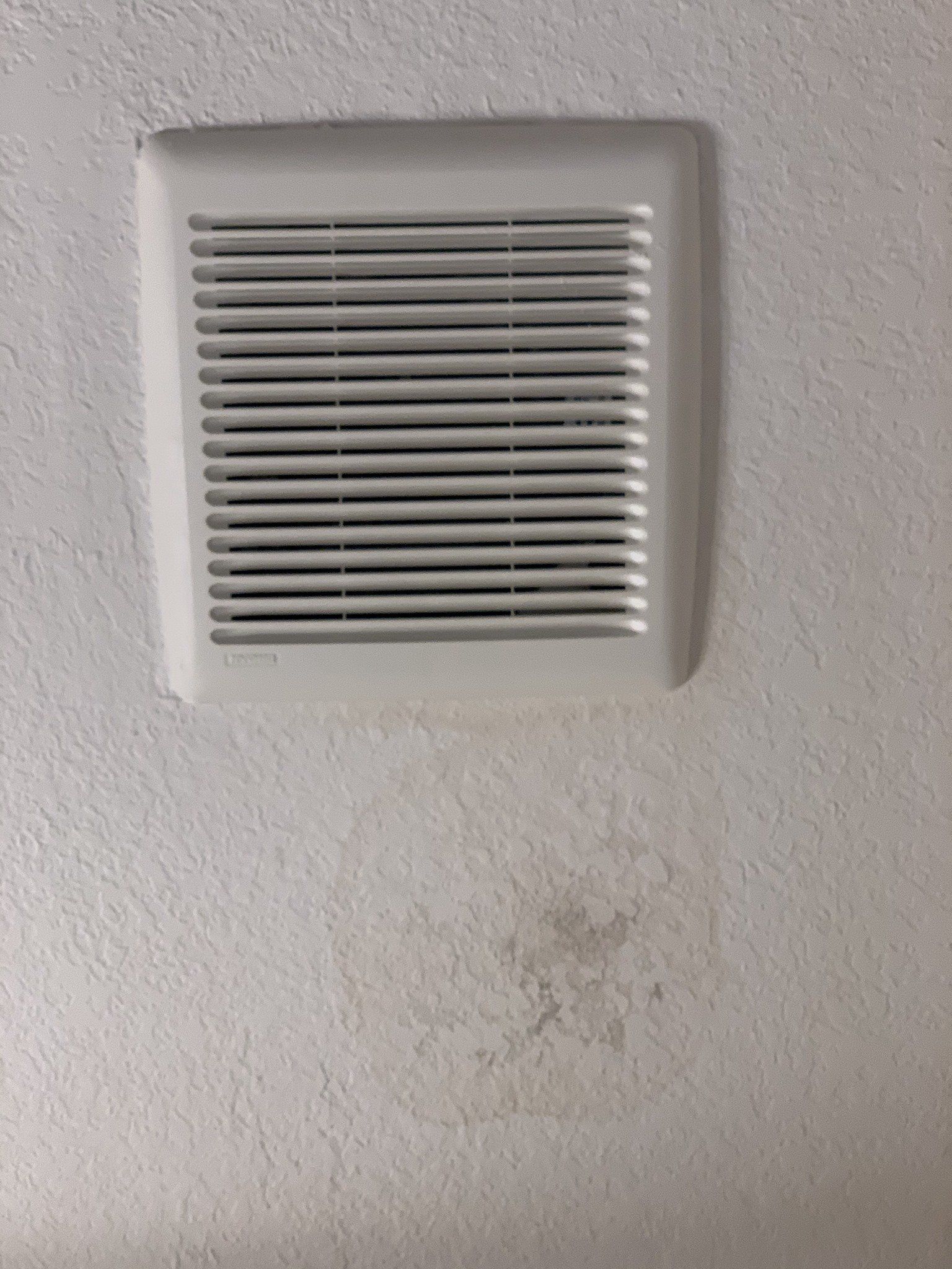 A white ceiling exhaust fan vent with a discolored, damp circular water stain on the ceiling surface below it.
