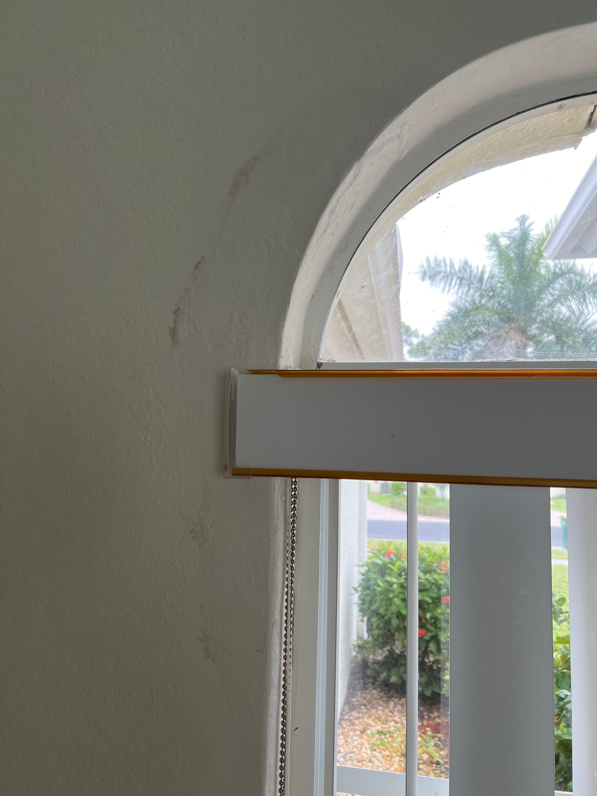 A close-up of a window frame with vertical blinds showing dark scuff marks or residue on the adjacent white wall.