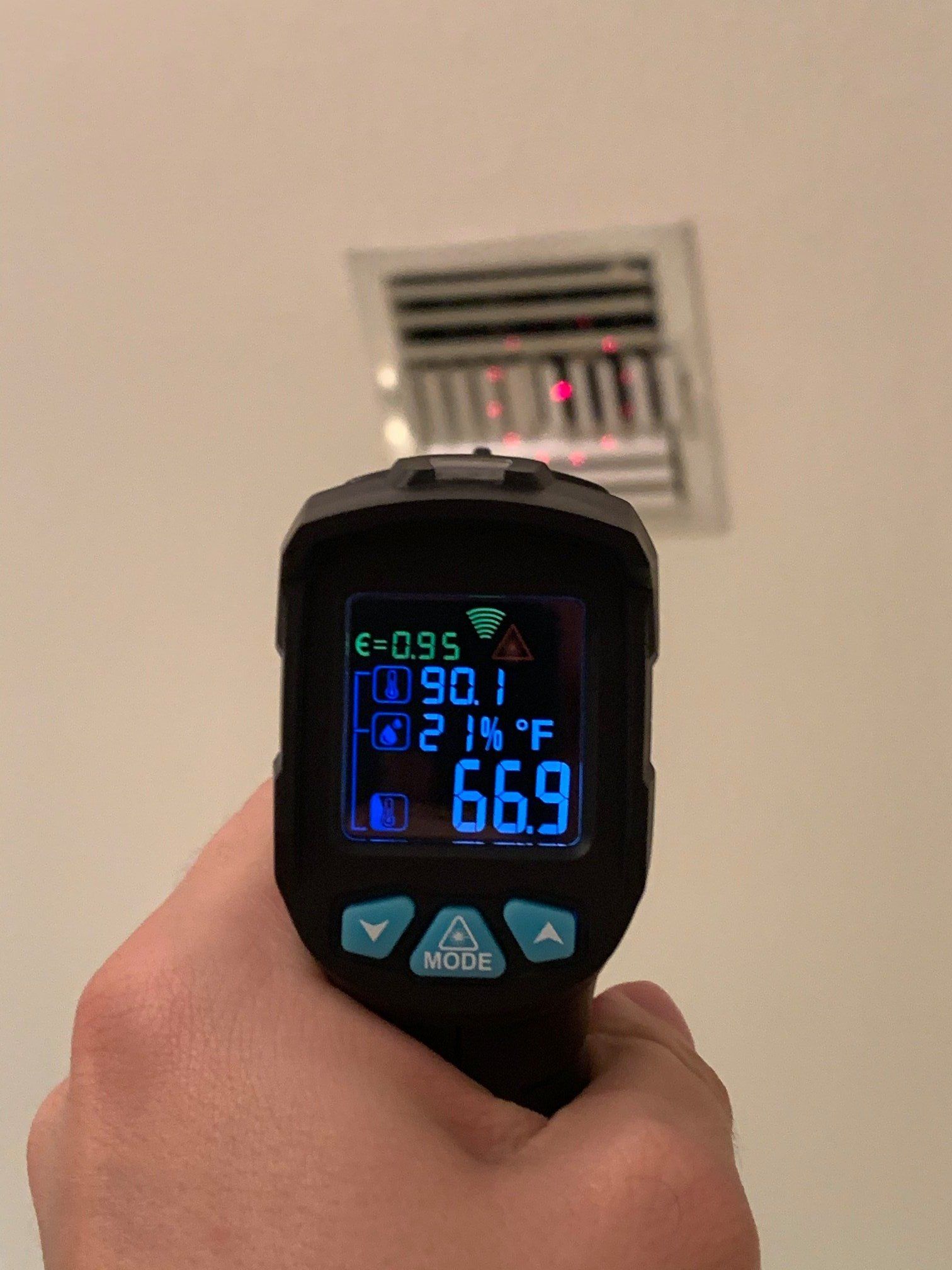 A hand holds an infrared thermometer pointed at a ceiling air vent, displaying a surface temperature reading of 66.9°F.