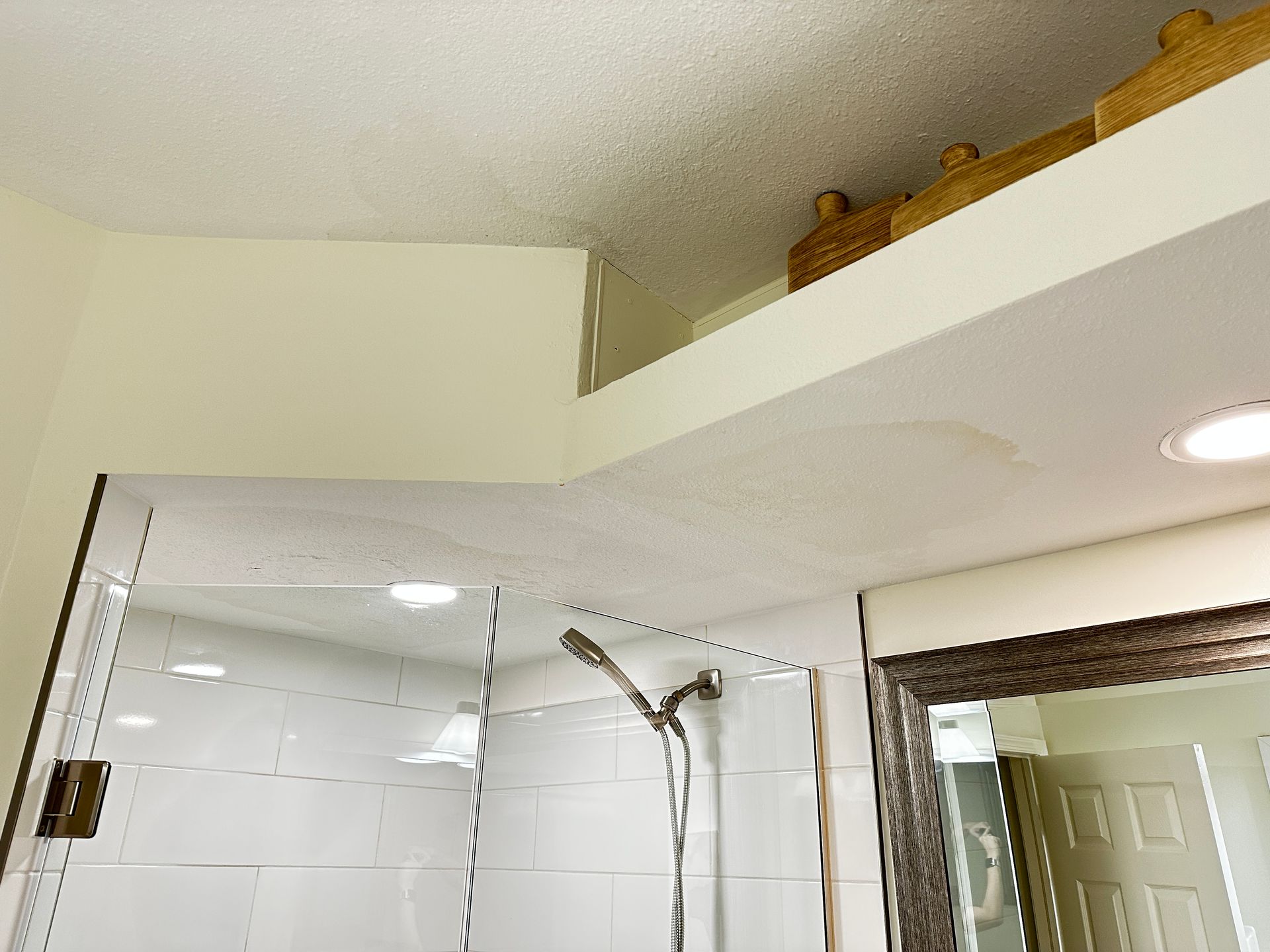 A bathroom view showing a shower enclosure with a glass door, a wall-mounted shower head, and a recessed ceiling ledge.