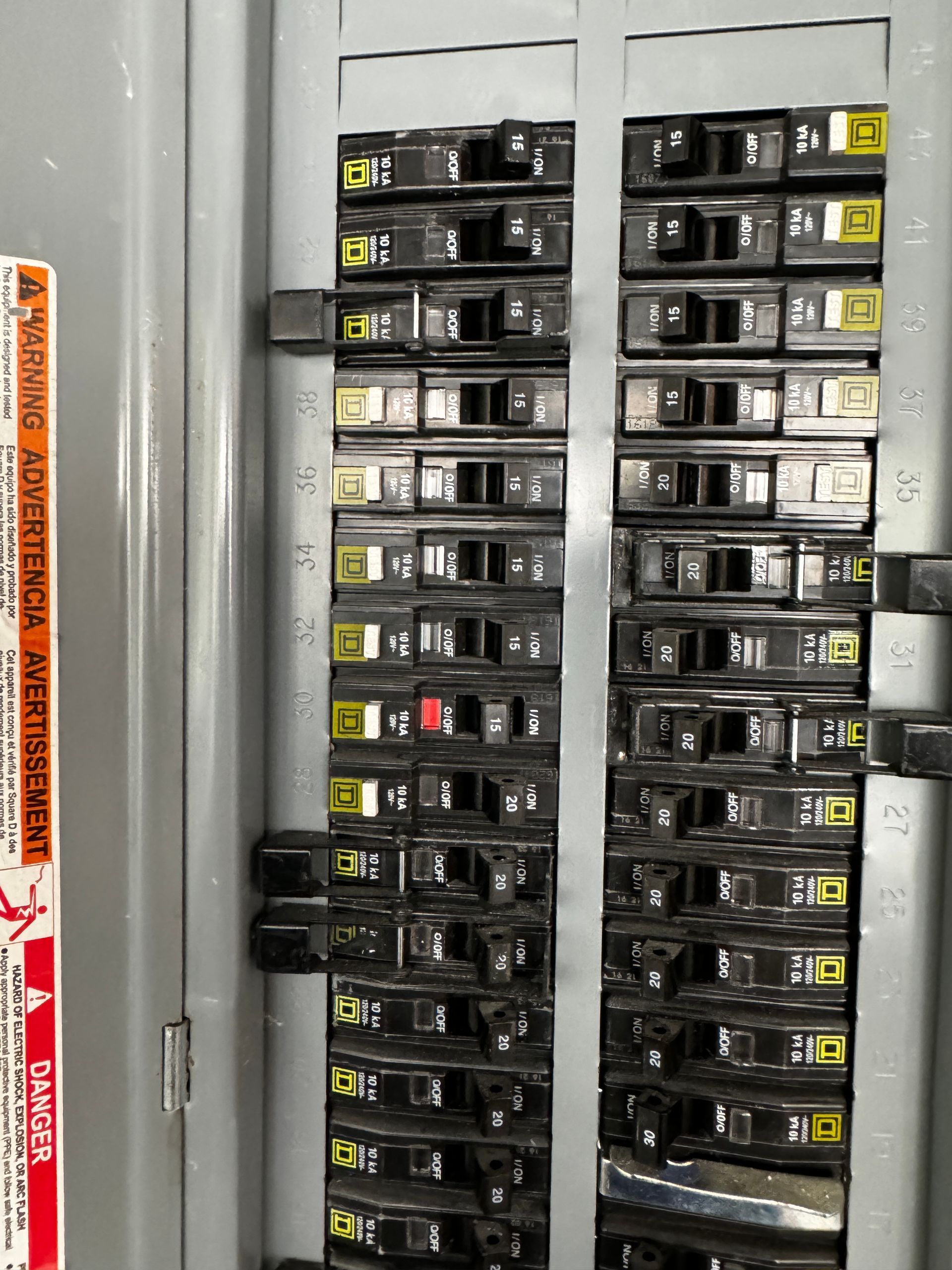 Electrical panel showing two rows of black circuit breakers with yellow labels and some switches in the off position.