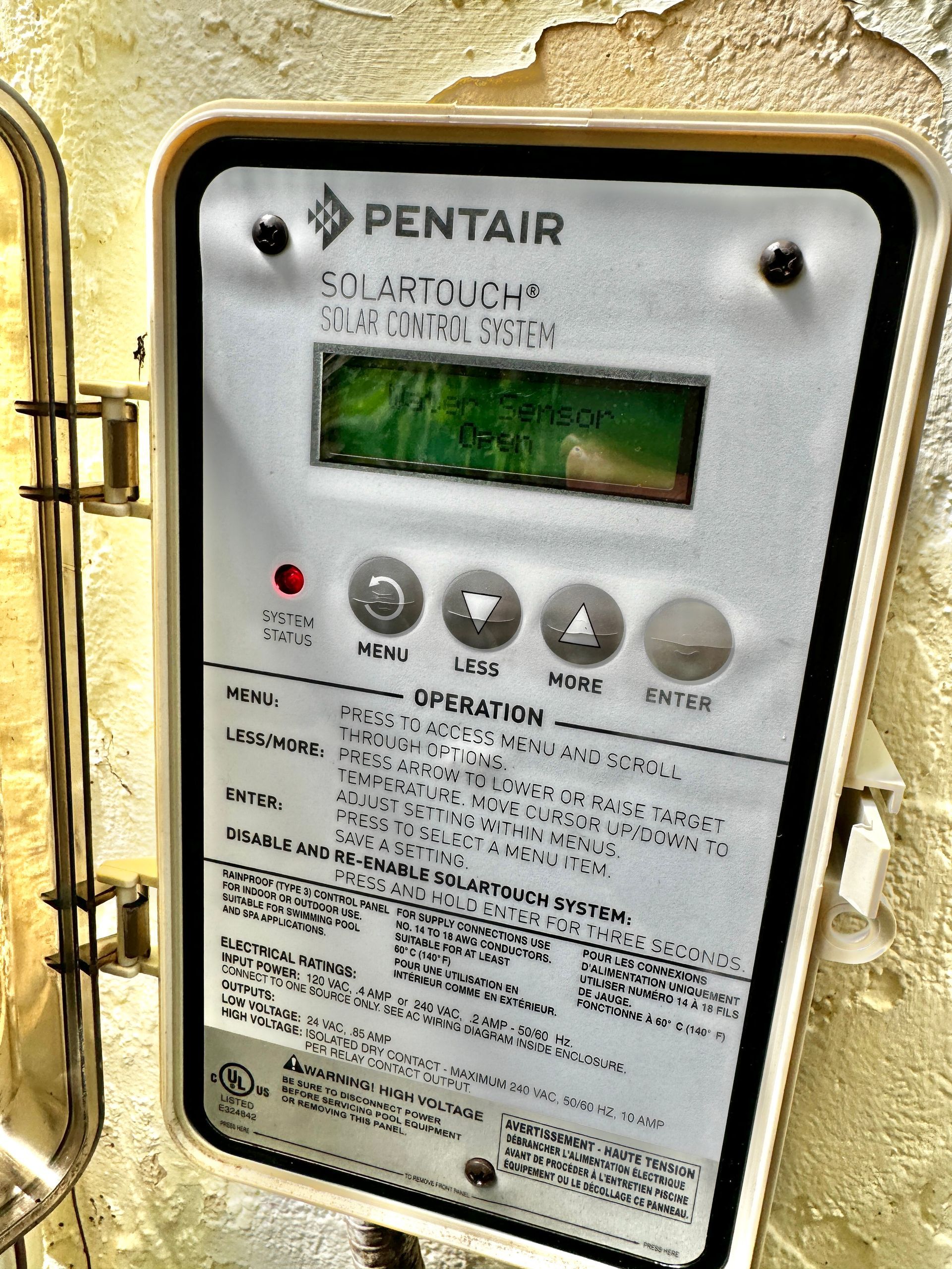 A Pentair SunTouch solar pool controller mounted on a textured wall, displaying information on its LCD screen.