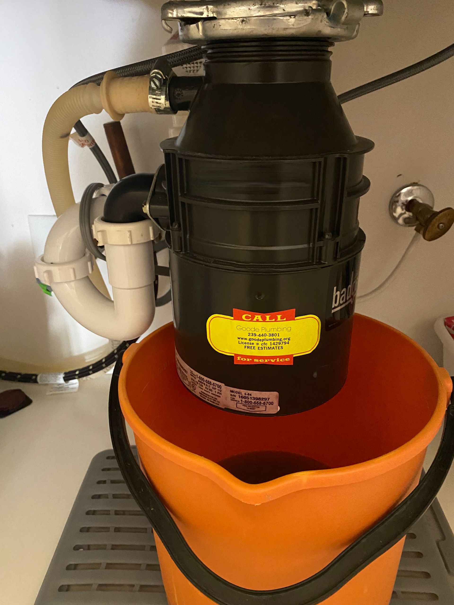 A kitchen sink garbage disposal unit positioned above an orange bucket to catch leaking water.
