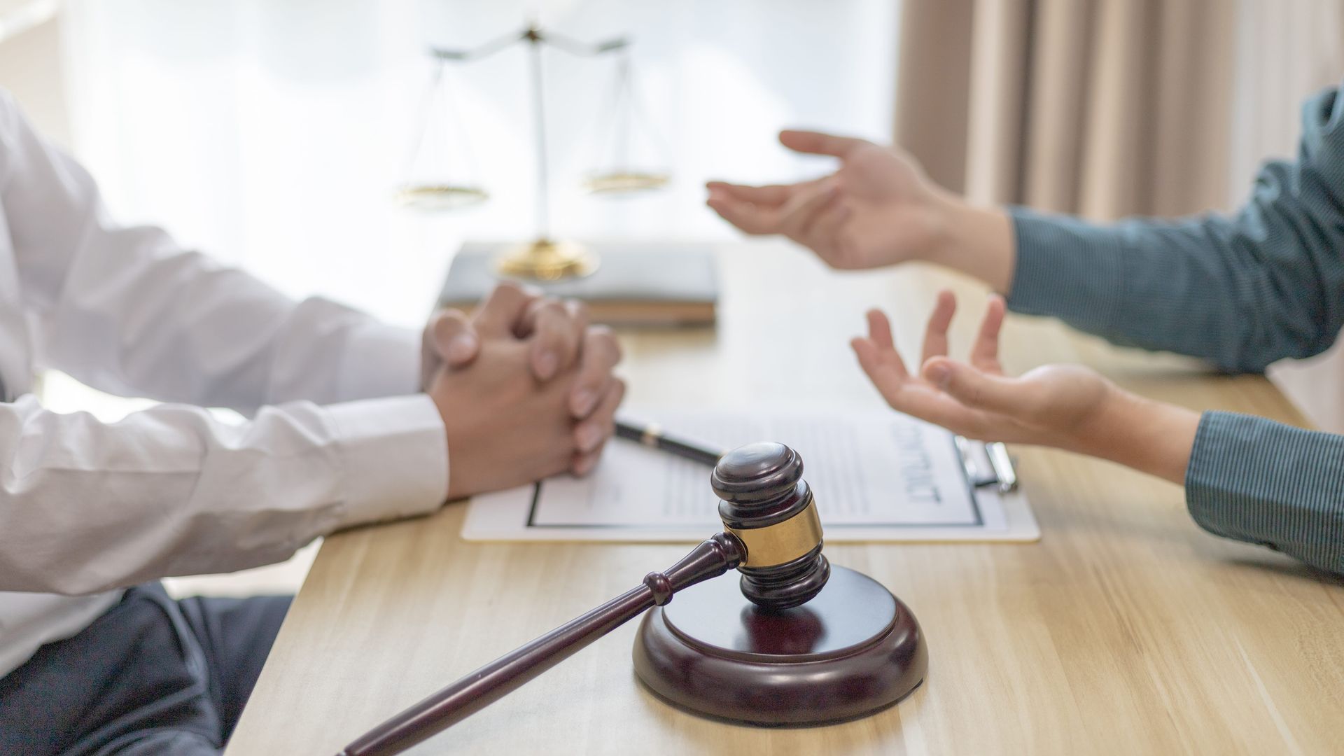 Lawyer and client discussing a case at a desk with a gavel and scales of justice in the background. 
