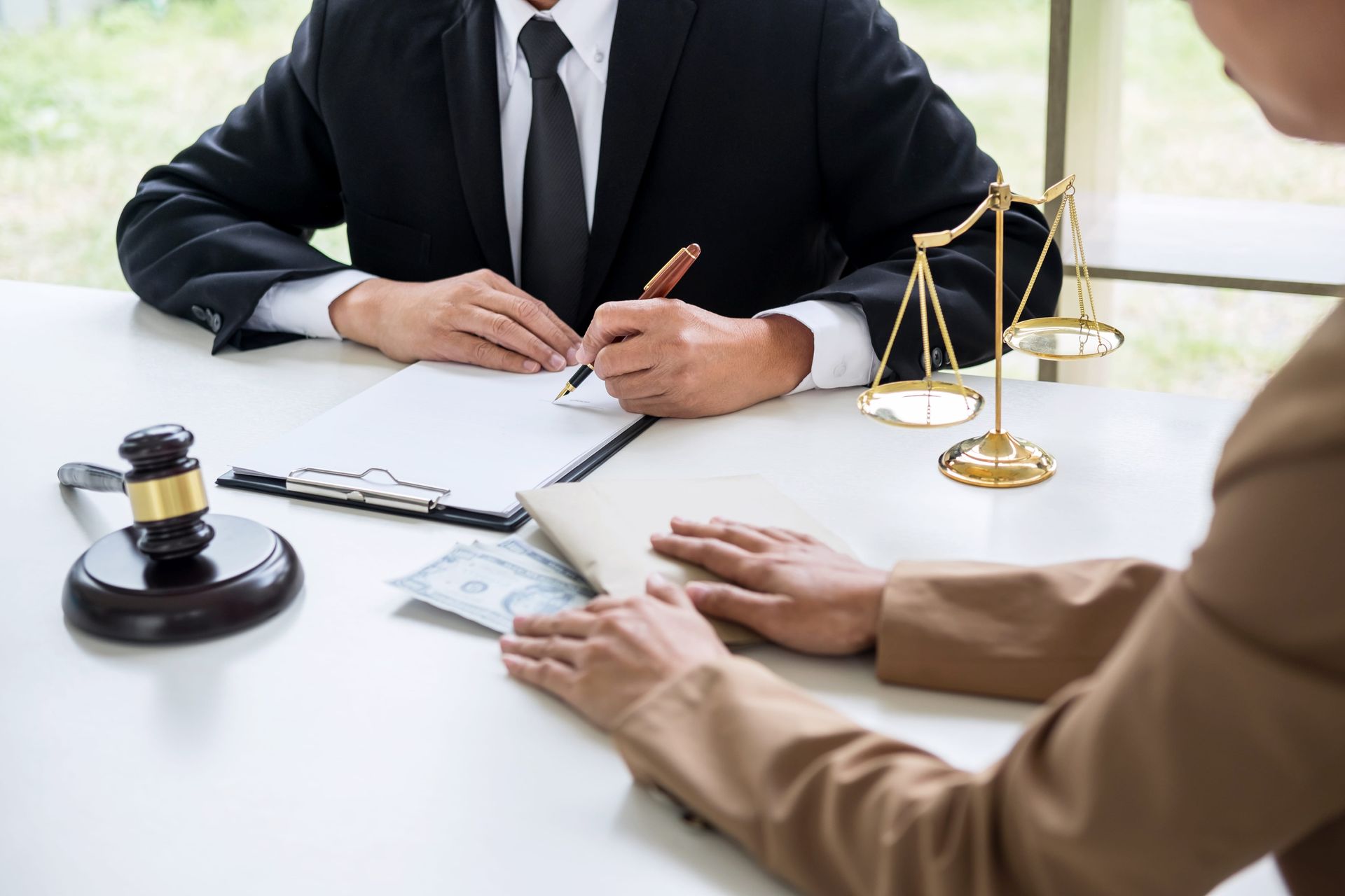 Lawyer meeting with client at desk, signing documents beside a gavel and scales of justice
