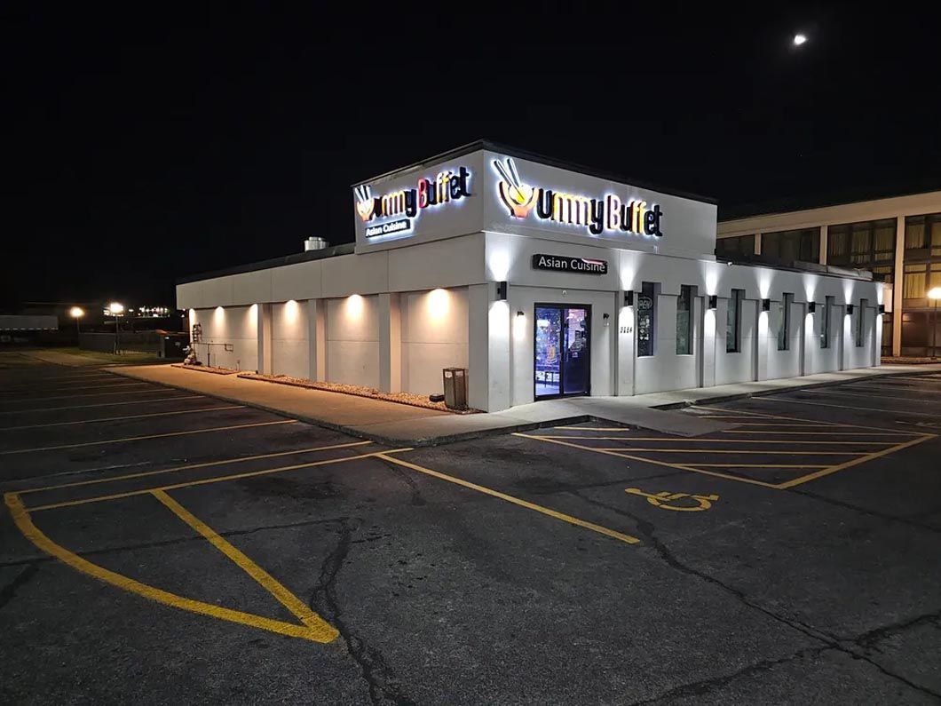 A large white building is lit up at night in a parking lot.