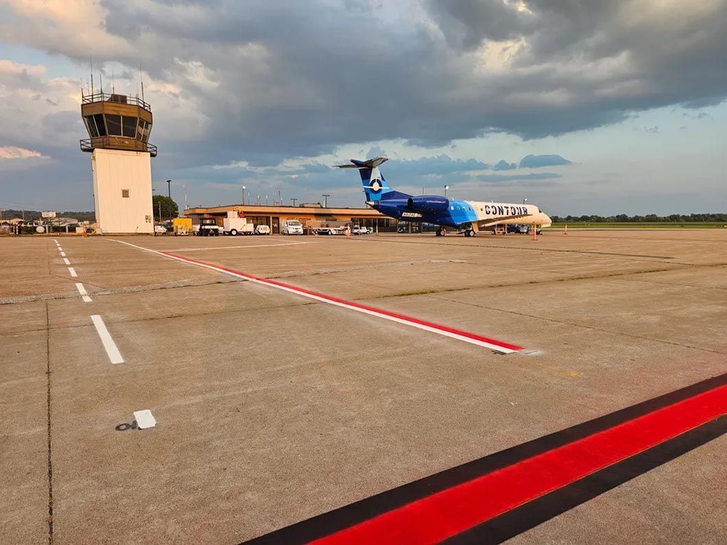 A blue airplane is parked on a runway with a tower in the background.