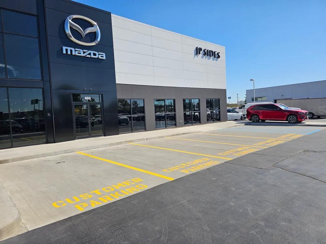 A red car is parked in front of a mazda car dealership.
