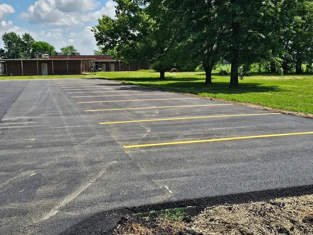 A parking lot with a building in the background and trees in the foreground.