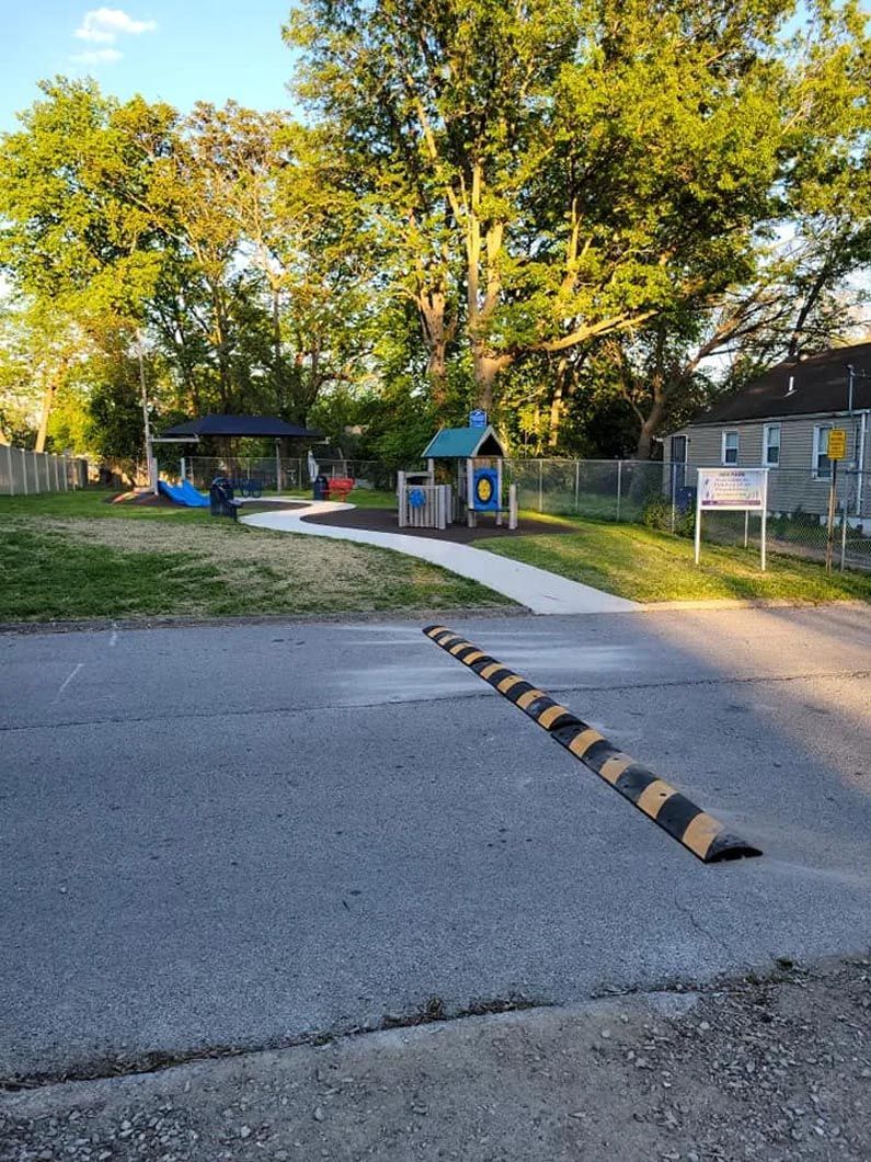A speed bump on the side of a road next to a park.