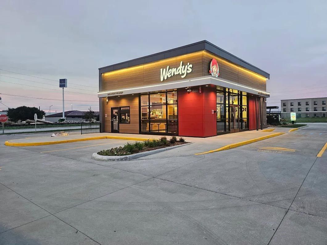 A wendy 's restaurant is sitting in the middle of a parking lot.