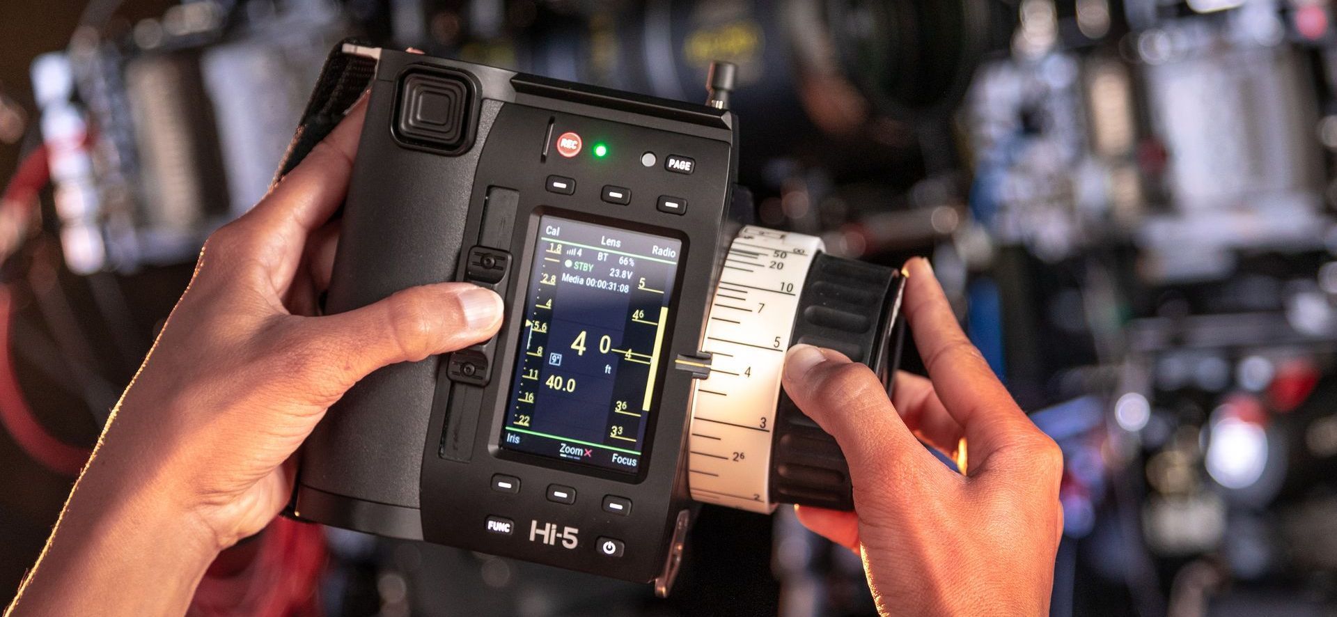Person holding a black camera, adjusting the lens, with a screen displaying data.