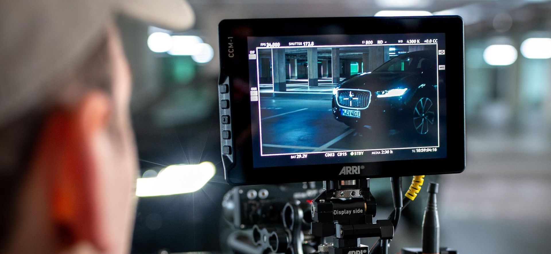 A person looks at a monitor showing a dark car in a parking garage.