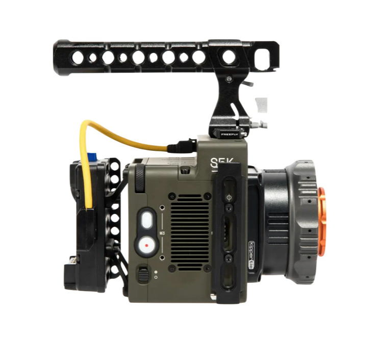 A professional video camera rig with handle and accessories; olive-green body, black rails, and orange lens ring.