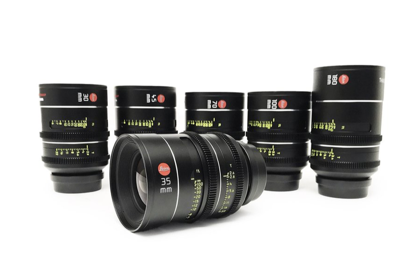 Five black cinema lenses, one in focus in front, the others behind, against a white background.