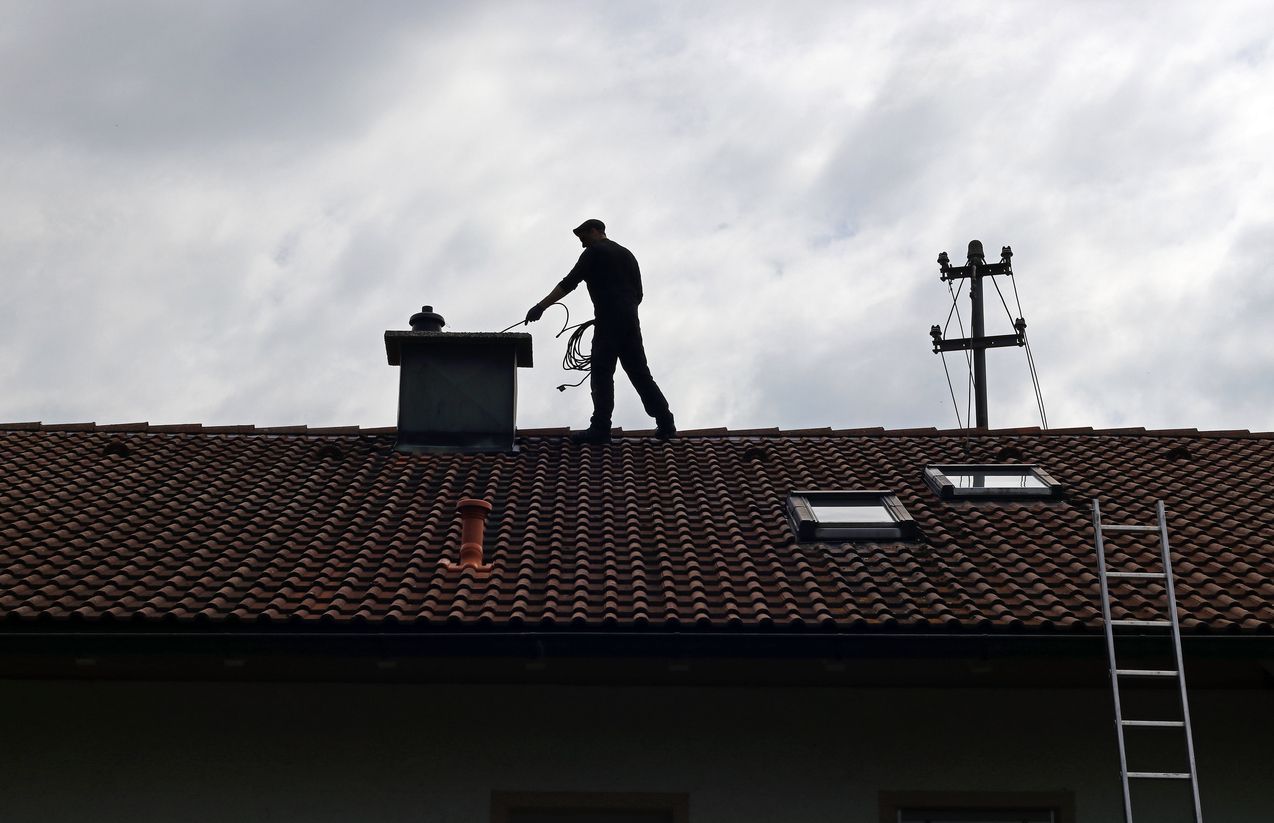 Silhouette of a roofer working on a tiled roof with a ladder and power lines at sunset
