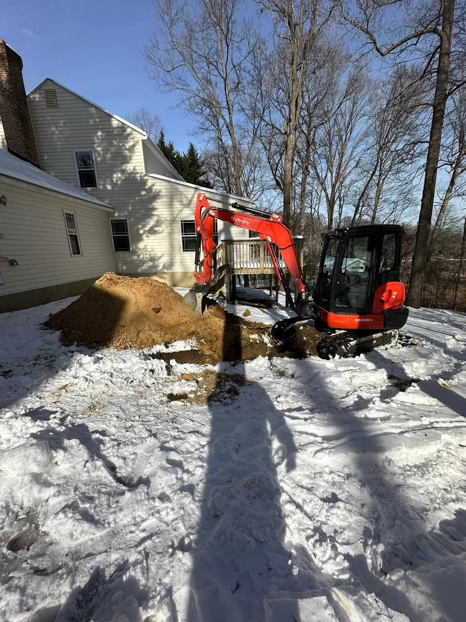An excavator is digging a hole in the snow in front of a house in Calvert County MD.