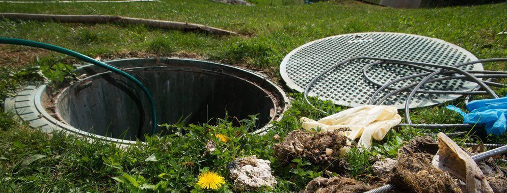 A septic cover is sitting on the grass next to a septic tank showing a septic pump out.