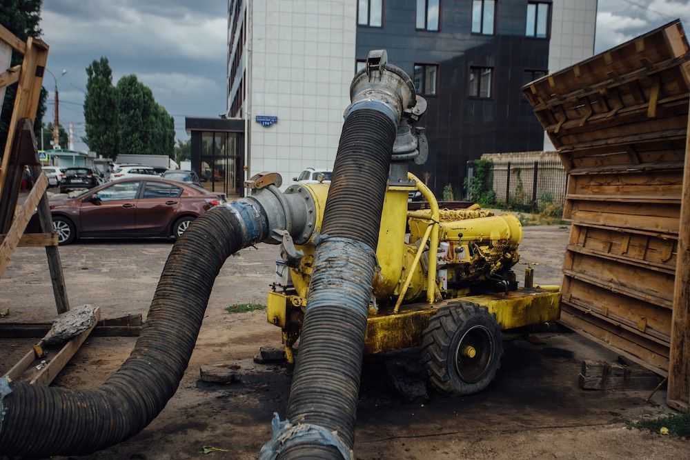A yellow pump with a large hose attached to it is sitting in a parking lot.
