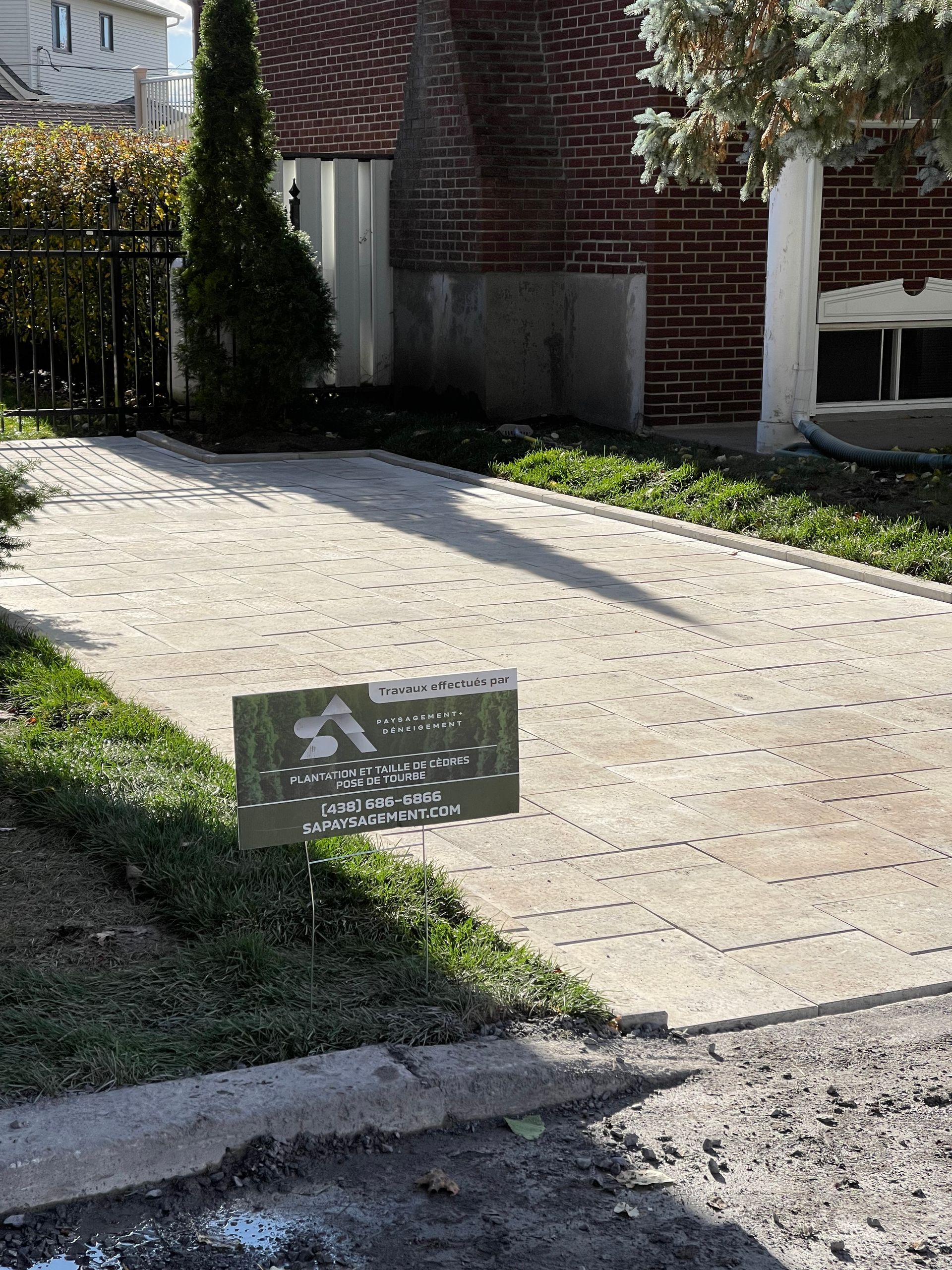 Chemin pavé, panneau dans l'herbe, bâtiment en briques.