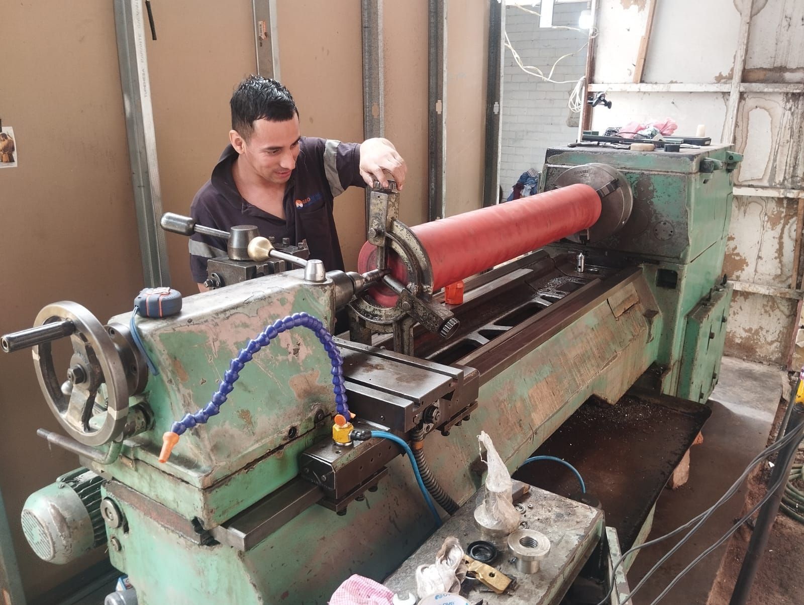 Persona operando un torno sobre una pieza cilíndrica roja en un taller.