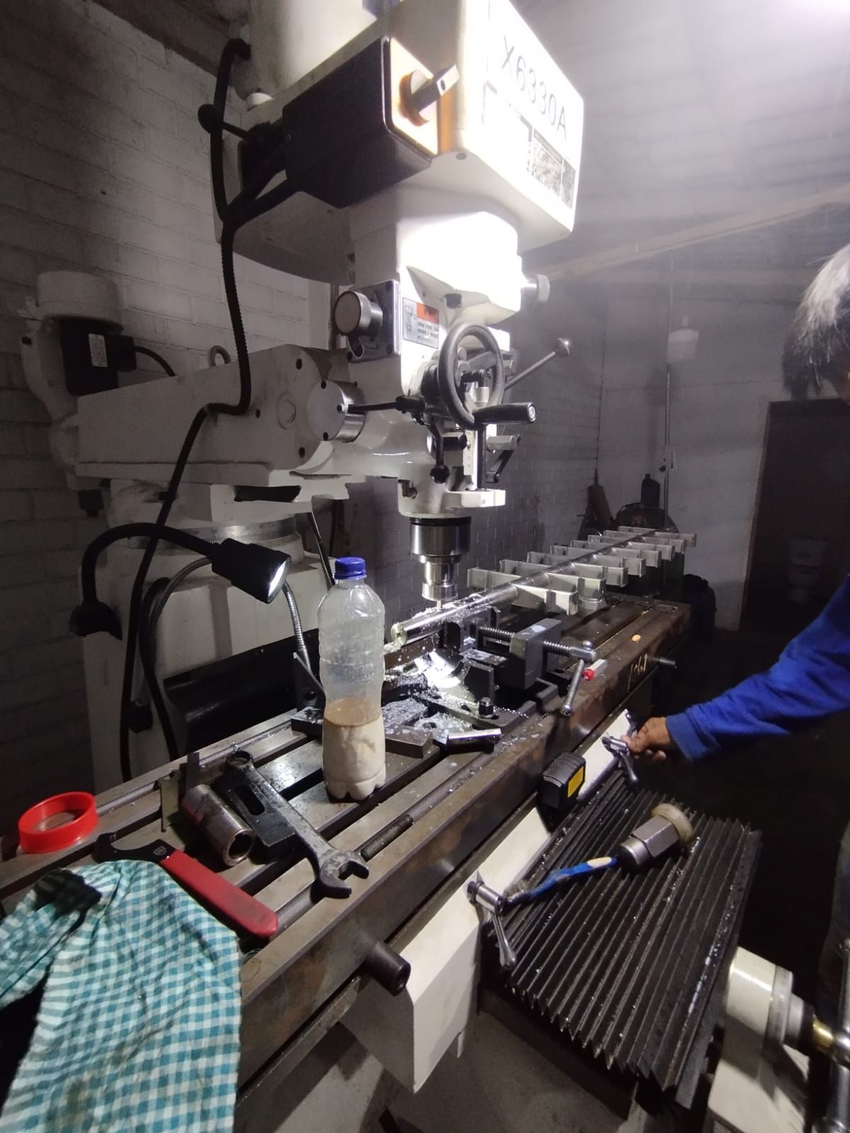 Taller industrial con una fresadora, herramientas y una persona con una chaqueta azul trabajando a su lado.