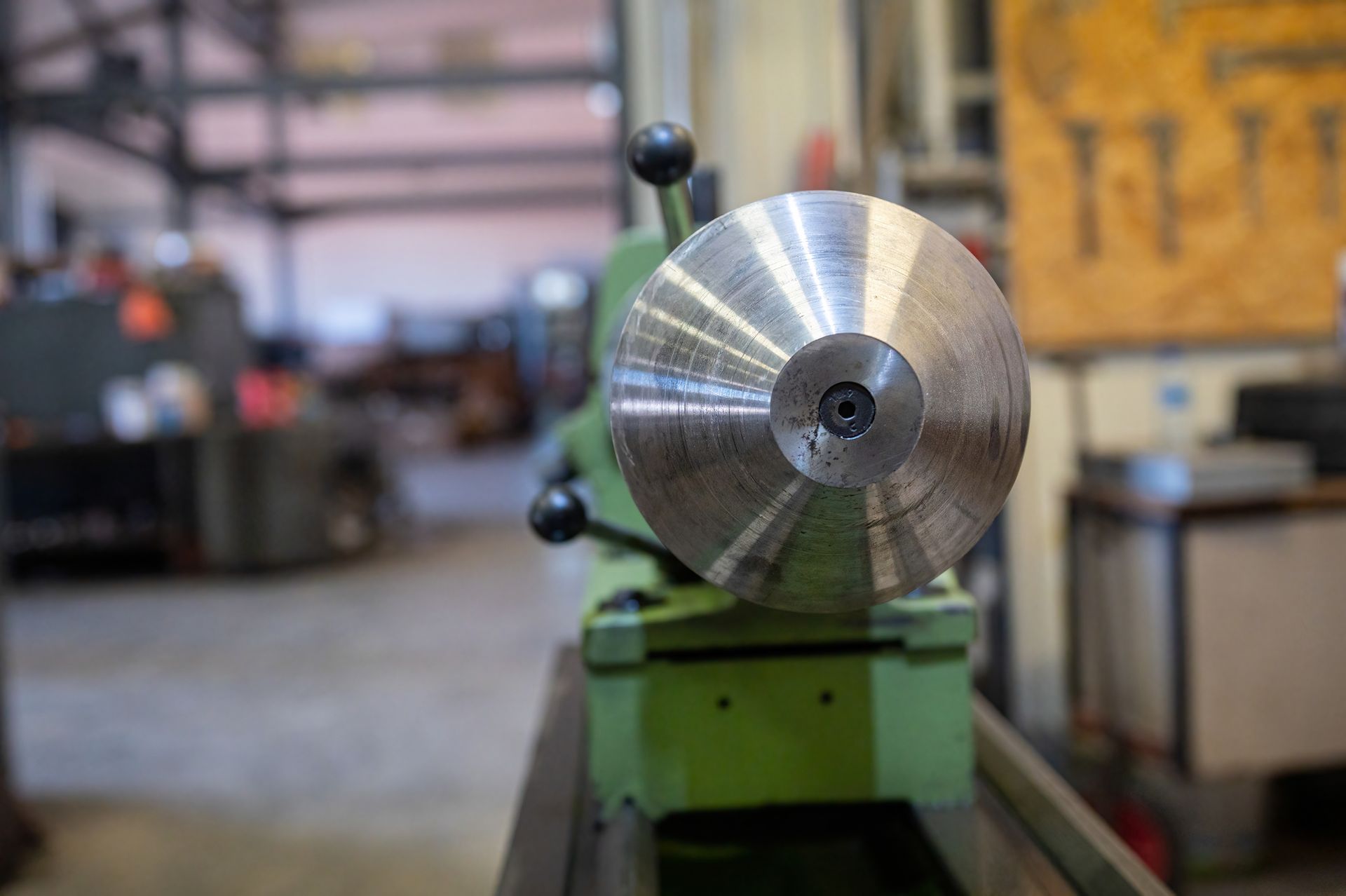 Torno de metal con una pieza de trabajo circular brillante en un taller, visto desde el frente.