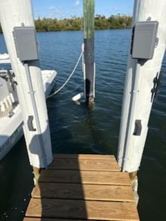 Wooden dock gate opening onto a calm blue waterway with pilings and shoreline in the distance