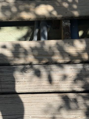 Wooden deck boards with dappled leaf shadows and a small view of the ground below through a gap