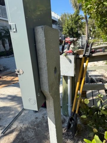Close-up of a utility pole and cable box with tools leaning nearby on a sunny sidewalk.