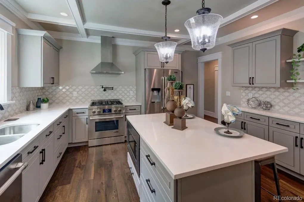 Modern kitchen with gray cabinets, stainless steel appliances, white countertops, and a central island.