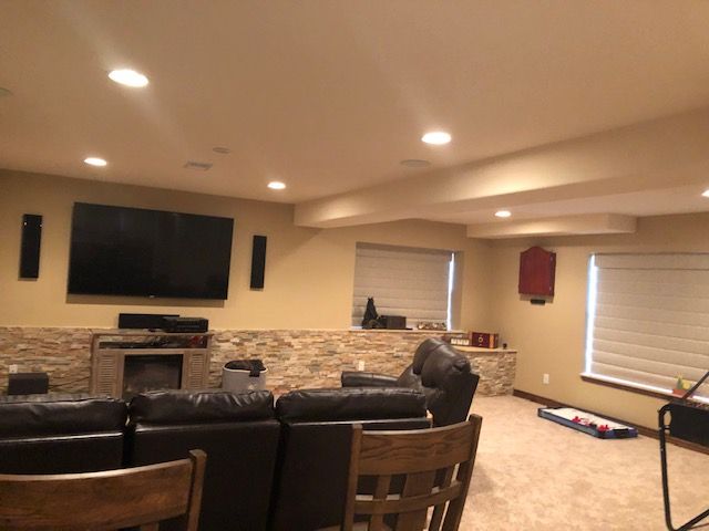A finished basement with a large TV, fireplace, and seating. Beige walls and carpet, recessed lighting.