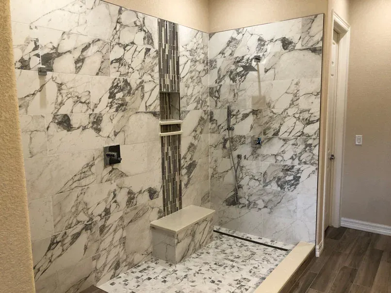 Marble-tiled shower with glass enclosure, pebble-stone floor, and built-in bench. A small door is visible on the right.