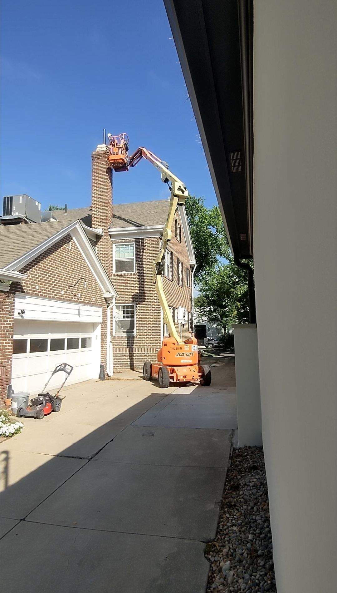 Orange lift truck near brick building, worker elevated, sunny day.