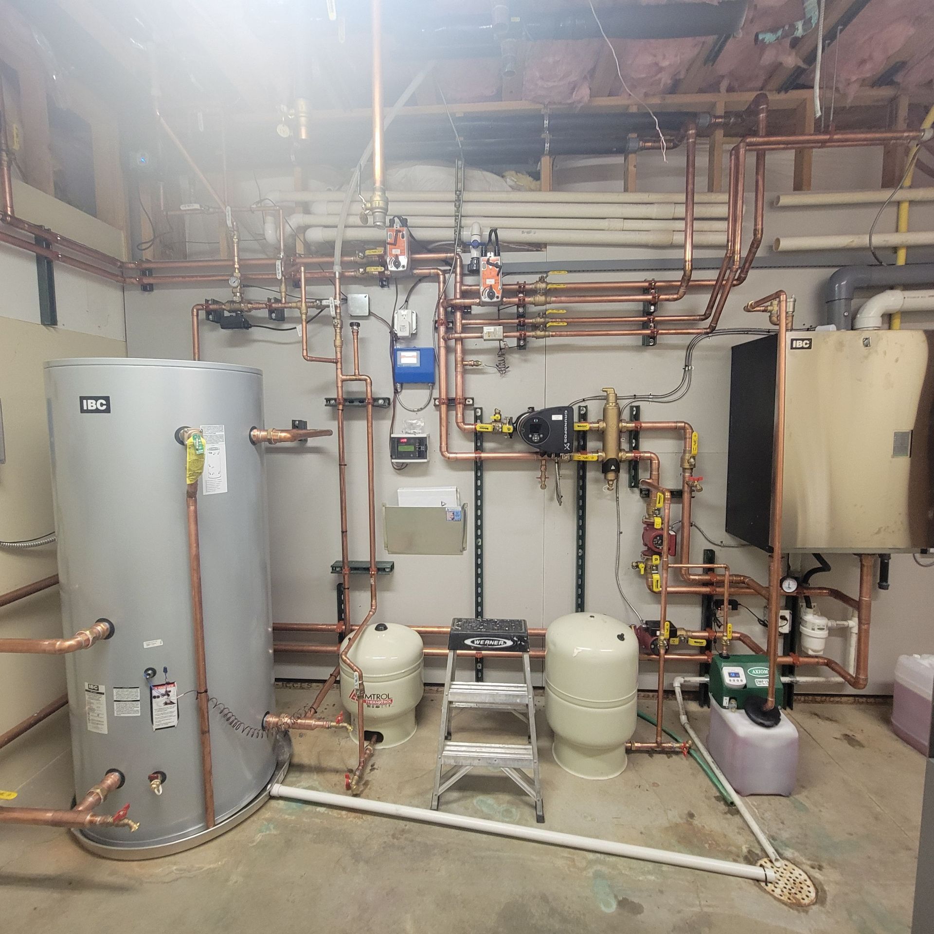 Plumbing system in a basement, featuring copper pipes, water tanks, and various equipment.