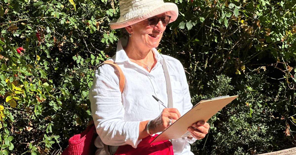 A woman in sunglasses and a hat outside in the sun, enjoying the workshop - with a pen and clipboard