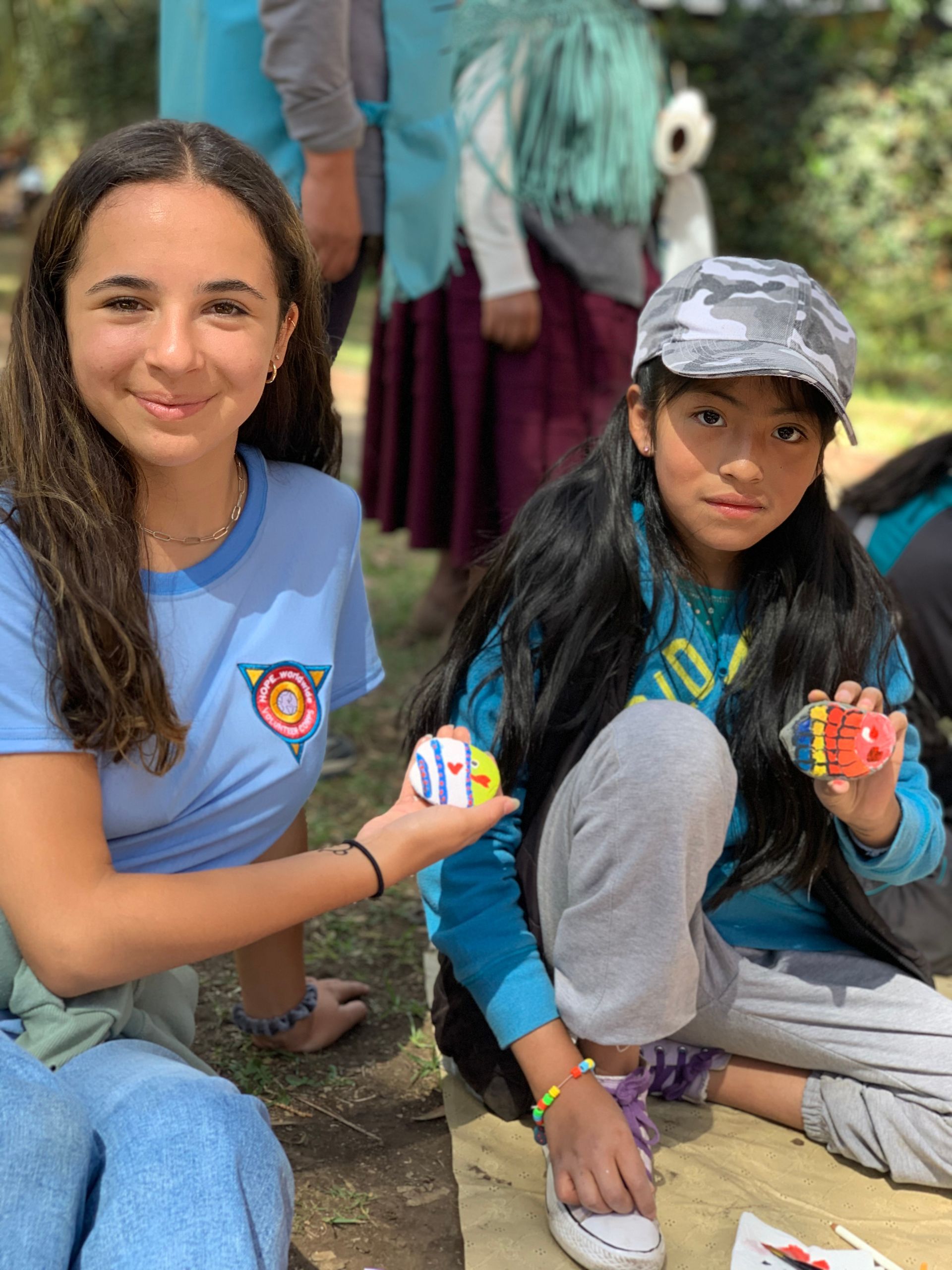 Two people crouch outdoors, smiling and holding colorful cup-stacking toys.