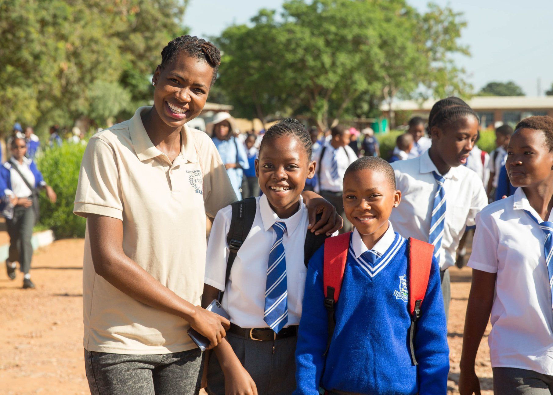 Teacher with smiling students outdoors in school uniforms on a sunny day
