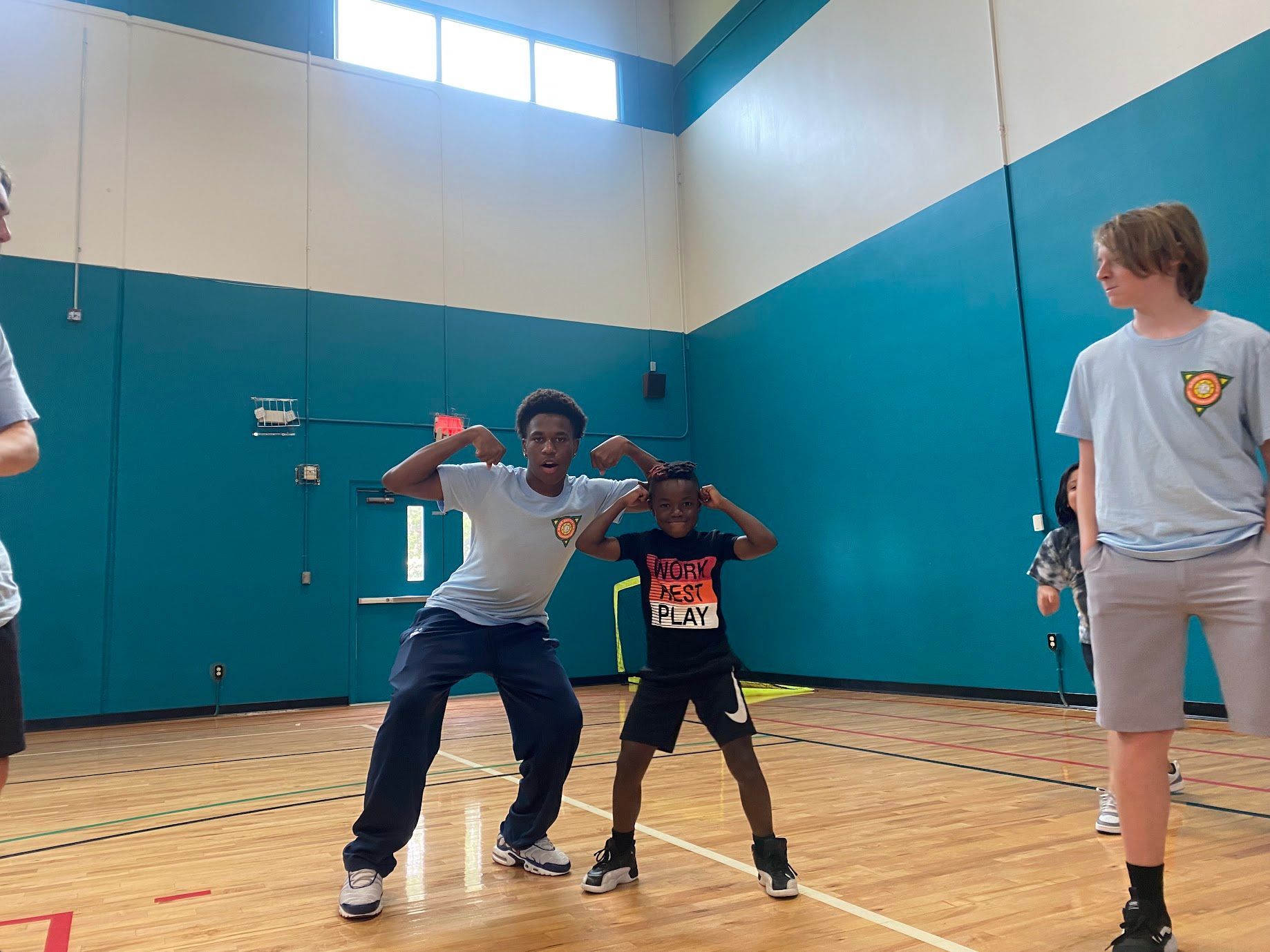 Two kids posing in a gym, with a third standing nearby against teal walls.