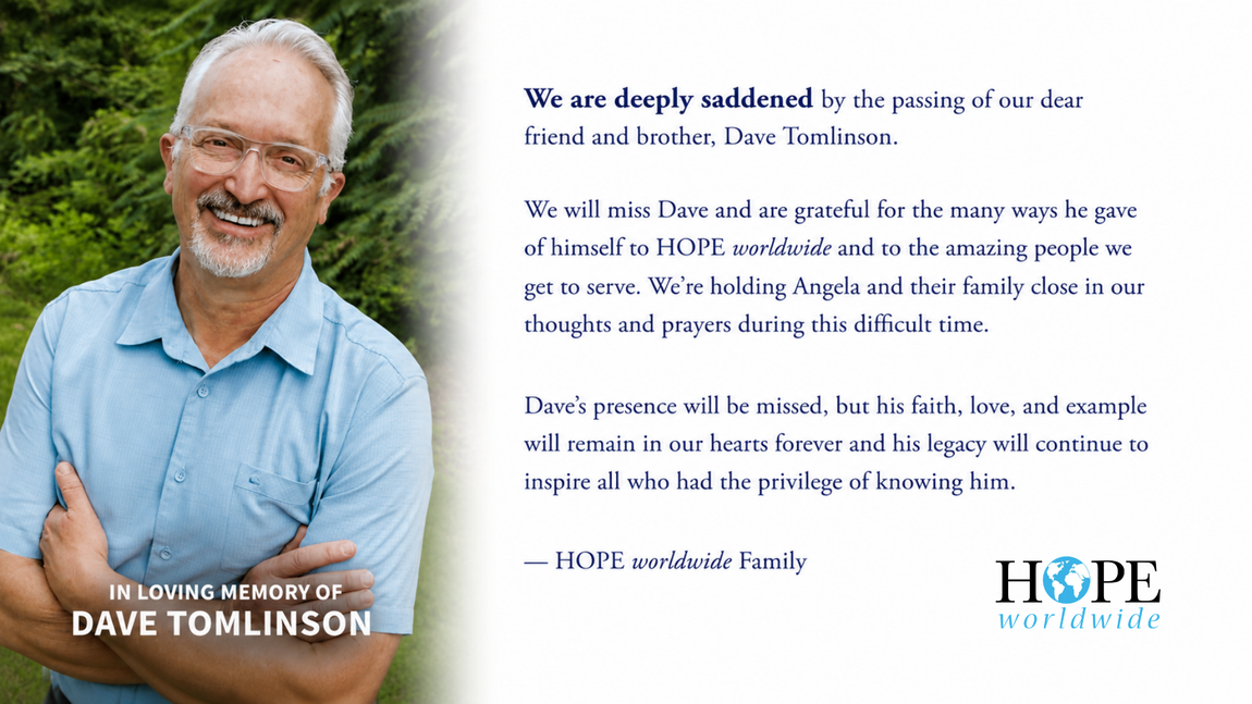 In loving memory of Dave Tomlinson, pictured smiling in a light blue shirt against a green outdoor background. A remembrance message honors his service to HOPE worldwide, his faith and lasting legacy, and offers prayers for his wife Angela and their family.